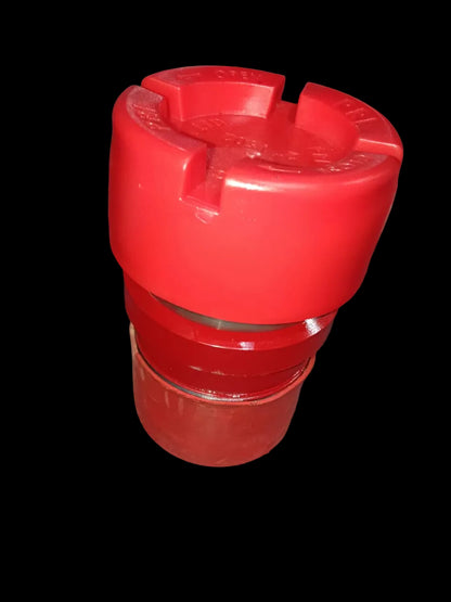 A red plastic cylindrical component with a threaded base and a ridged top section, photographed on a dark workshop floor.